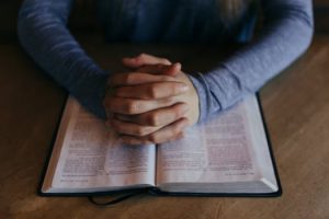 folded hands laying on top of what appears to be a Bible