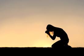 person bowing on their knees with head down, hands in prayer position