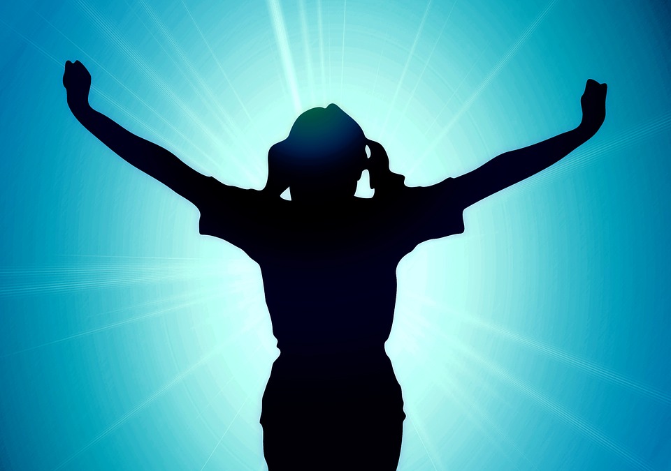 silhouette of a girl with arms raised against shining light on blue wall