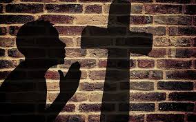 shadow on a brick wall of man praying at the cross
