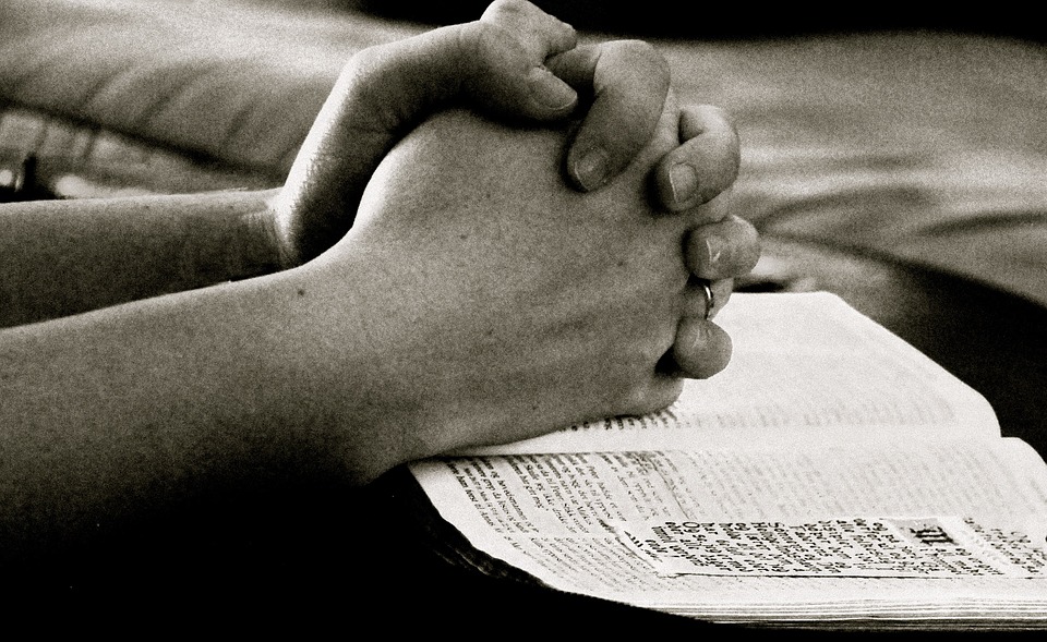 folded hands resting on an open Bible