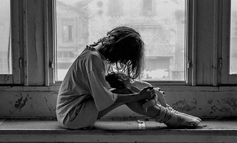 black and white photo of person sitting against window, side view, with head down on knees feeling guilty