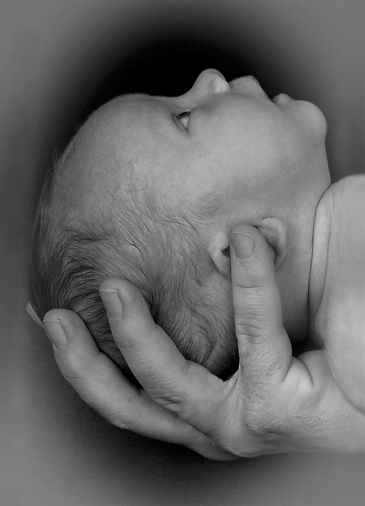 A baby's head being cradled by a large hand with baby looking up