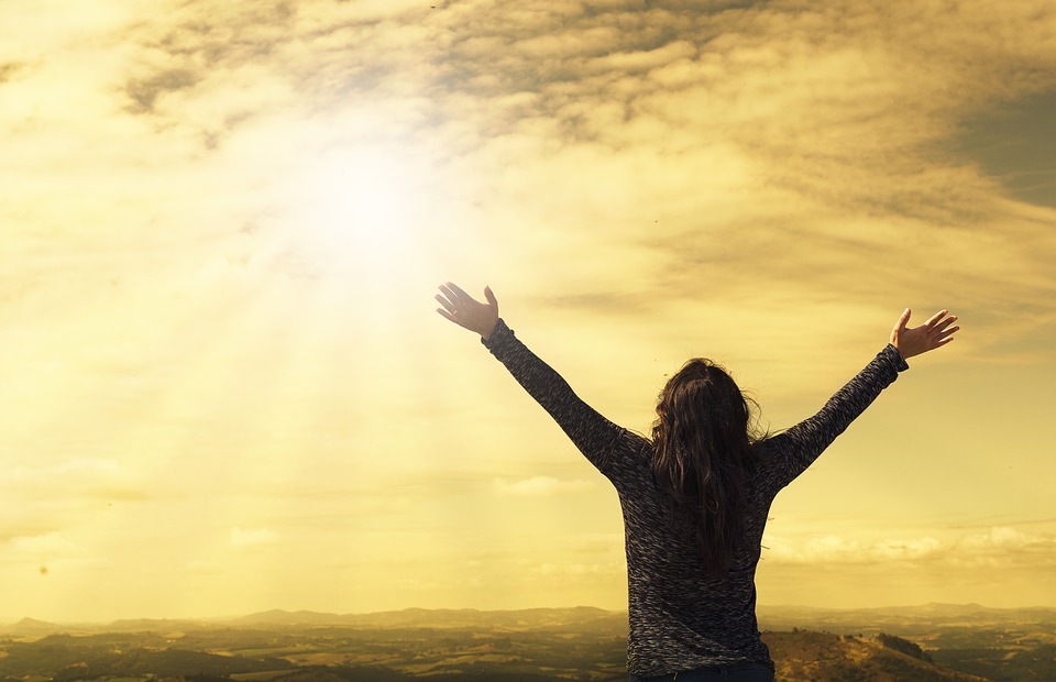 person standing with arm reaching up facing the sun and sun beams