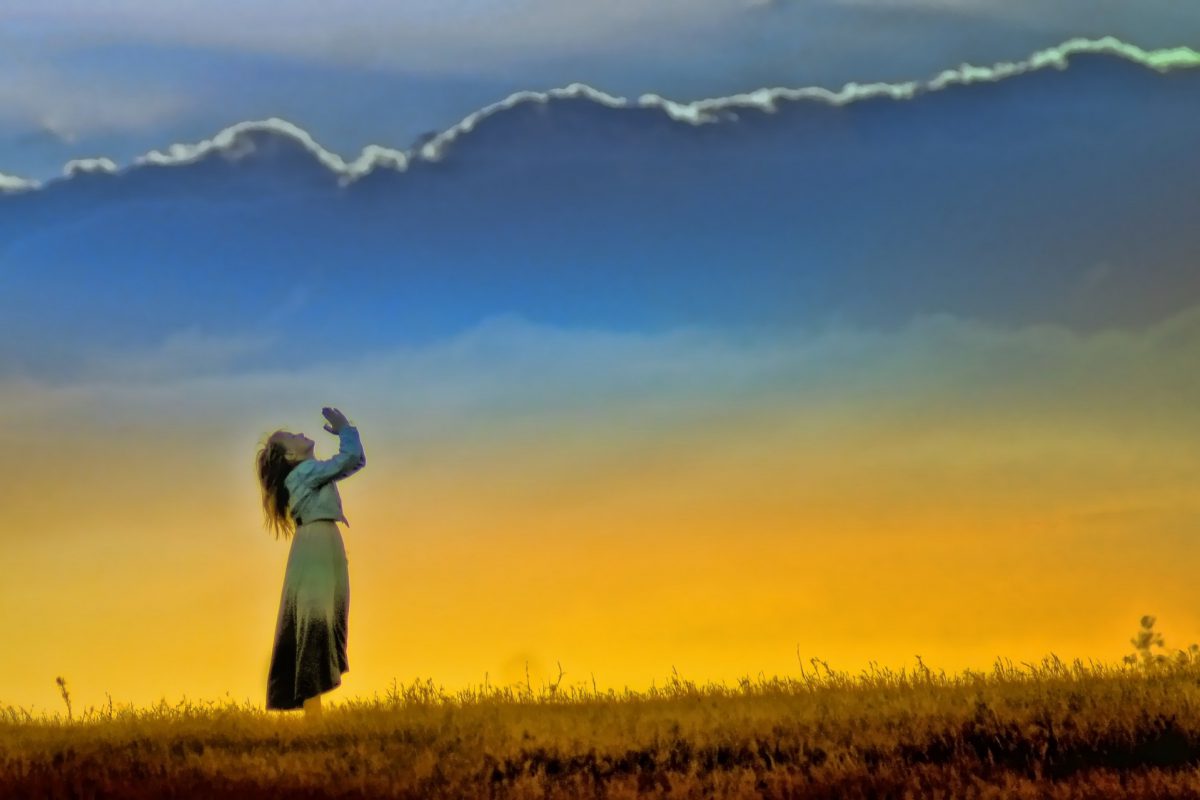 woman raising her arms in praise to God with sunset in the background