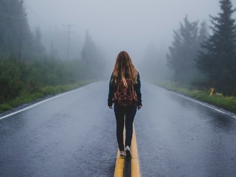 girl walking down a road into fog, with her back to us, 