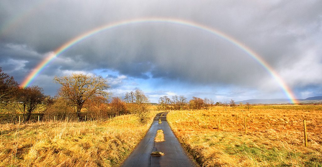 deserted country road with a rainbow in the distant horizon