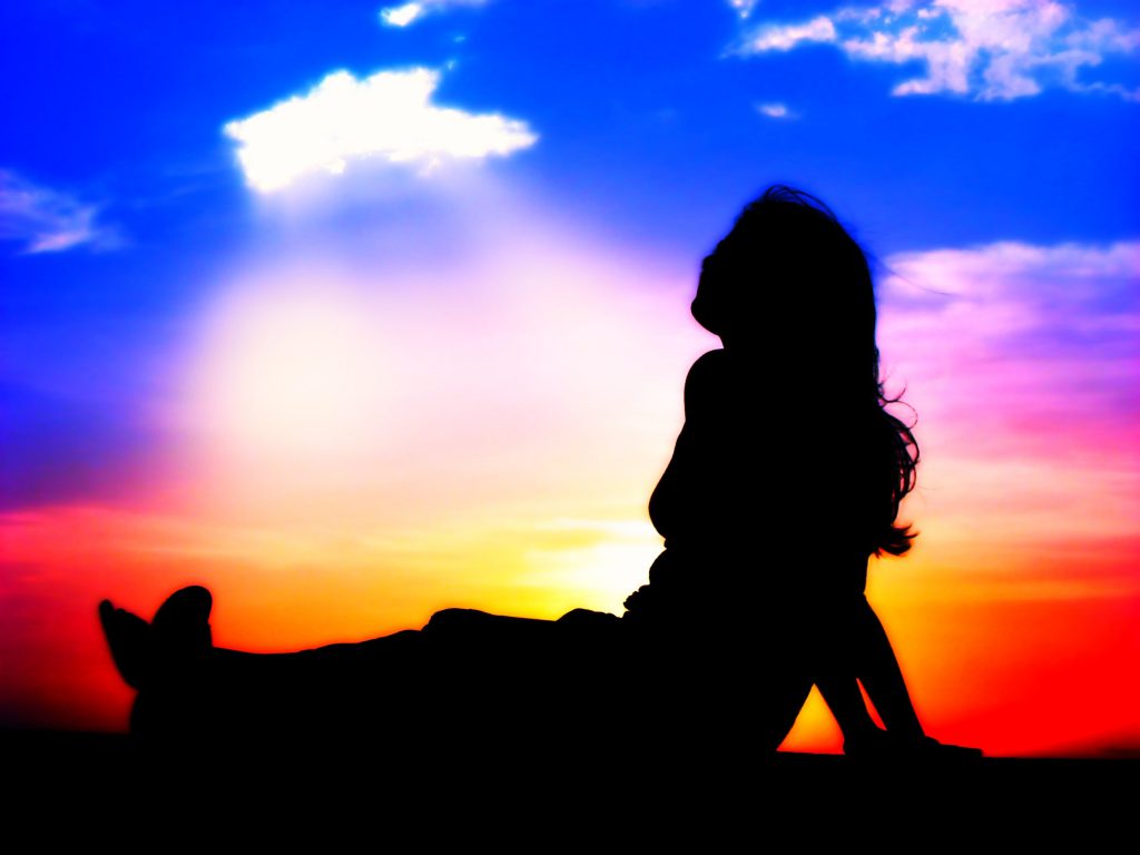 silhouette of a girl looking up to a whole in the sky at sunset
