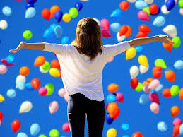 woman with arms outstretched looking at a blue sky full of floating balloons