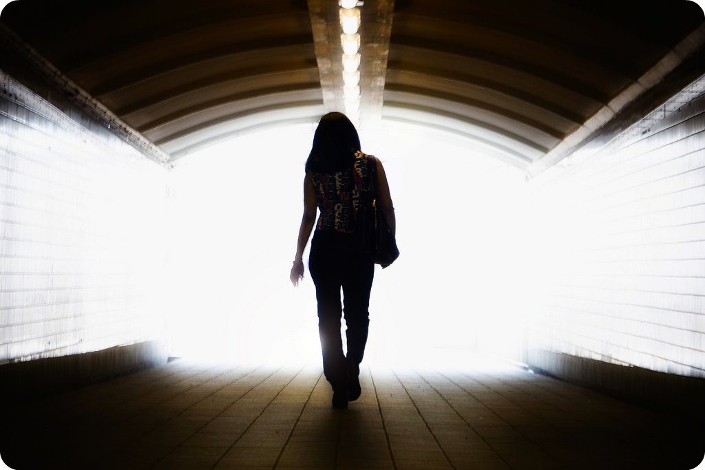 Woman walking into a tunnel with bright lights at the other end