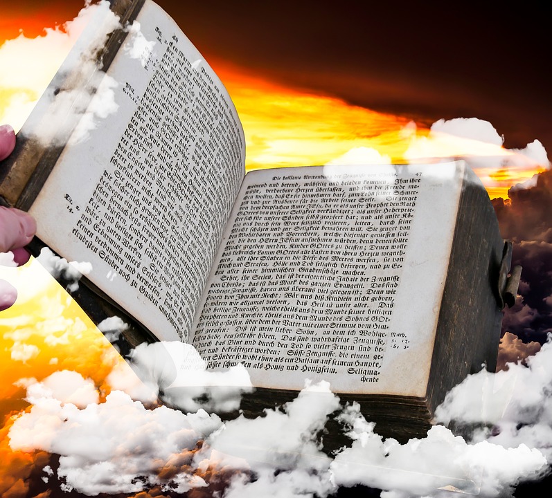 An old Bible opened with cloud superimposed around it on a sunset background
