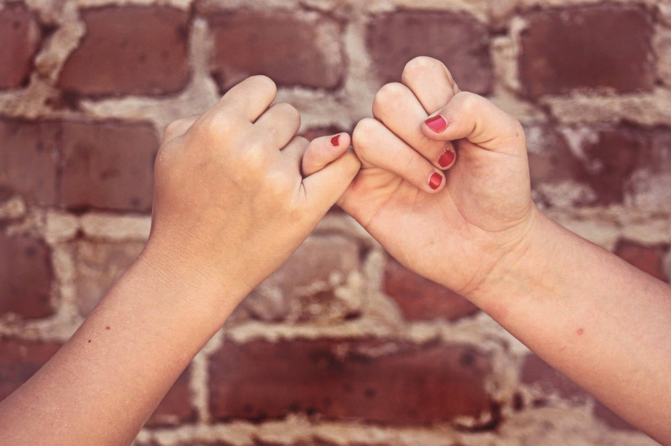 pinky promise with two pinky fingers locked together with brick wall background