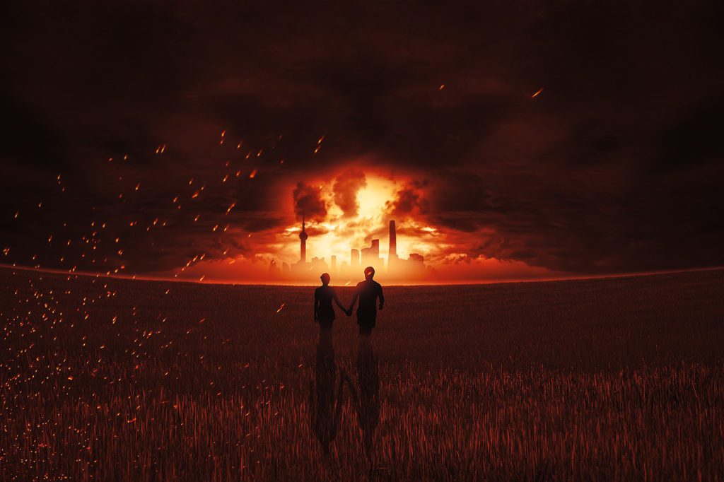 Two people holding hands, at night, looking at what looks like an explosion in a city in the distance ahead of them