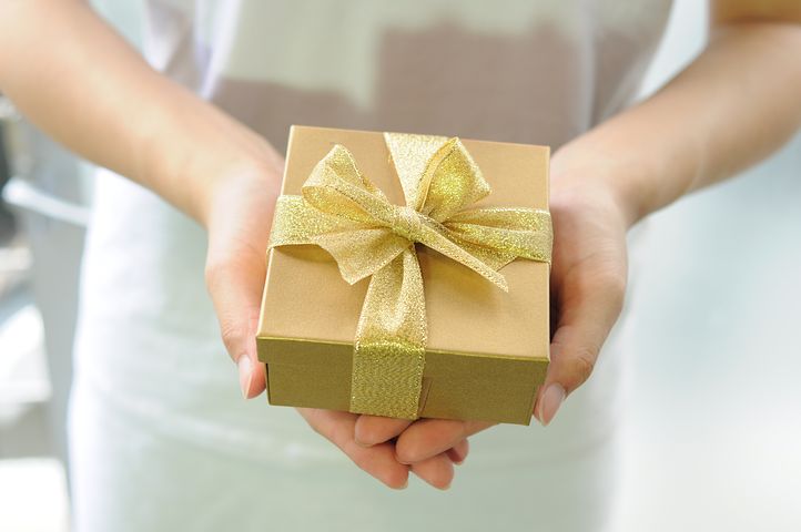 hands holding a gift wrapped in gold paper with gold lace bow