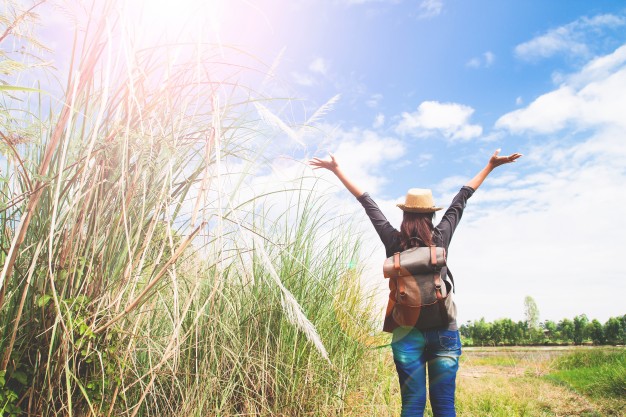 woman standing in the field with her arms reaching toward the sun