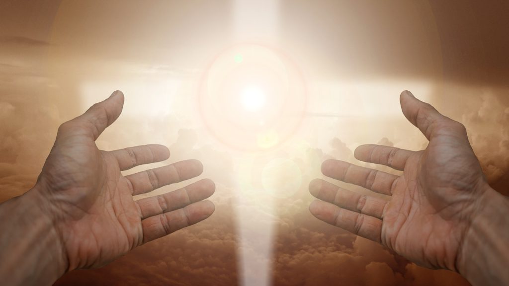 two hands extending toward a bright light in the shape of a cross