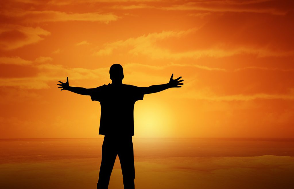 man with his arms outstretched facing a yellow and orange sunset