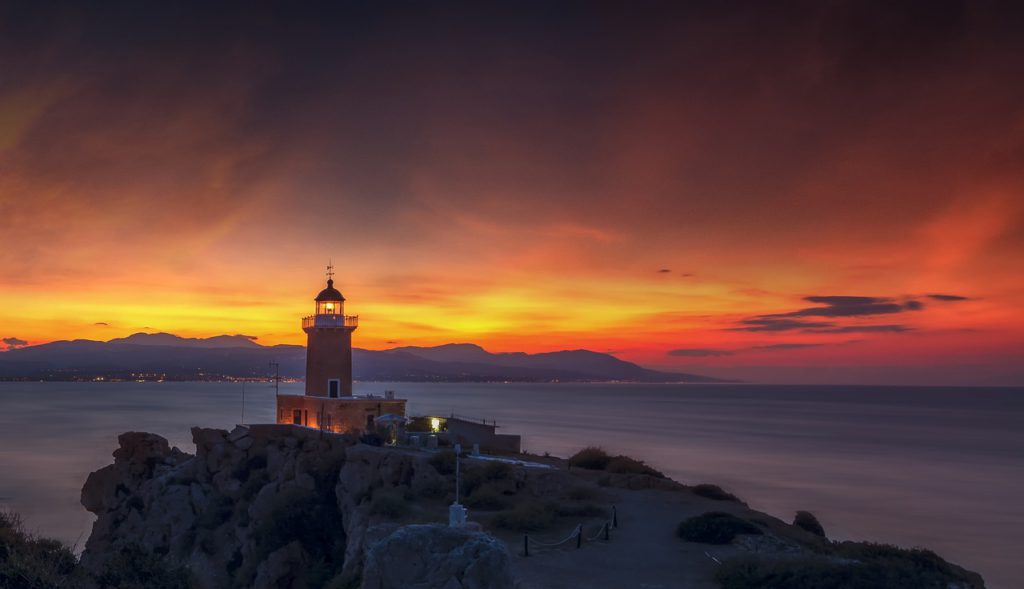 lighthouse overlooking a bay, with a sunset in the background
