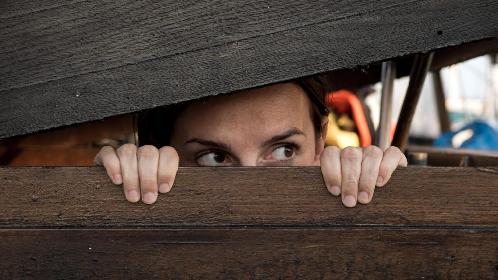 someone peering out between a crack in a wooden fence like they are hiding and on the look out