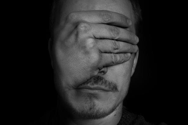 black and white image of a man covering his eyes, set against black background