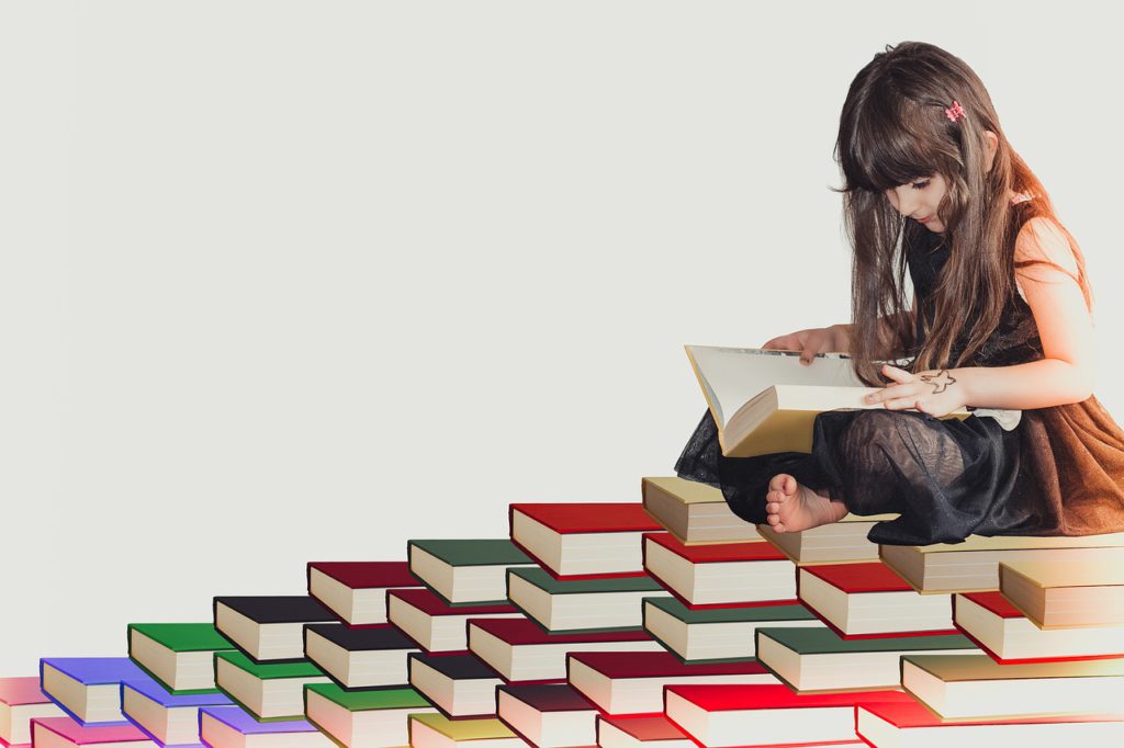 little girl reading a book while sitting on a pile of books