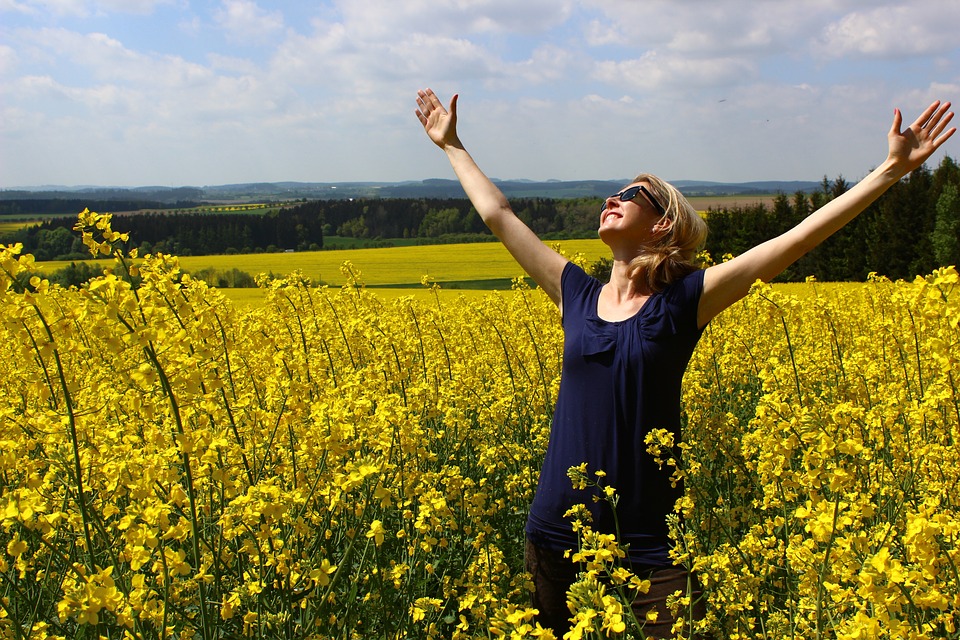 woman reaching her arms up, looking up, praising, in field of yellow flowers