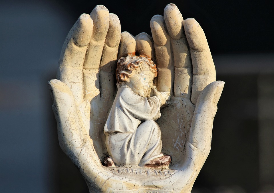 statue of small person huddled in and surrounded by larger hands cupped around it