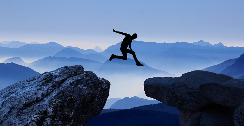 man jumping from ledge to ledge, mountains in the distance