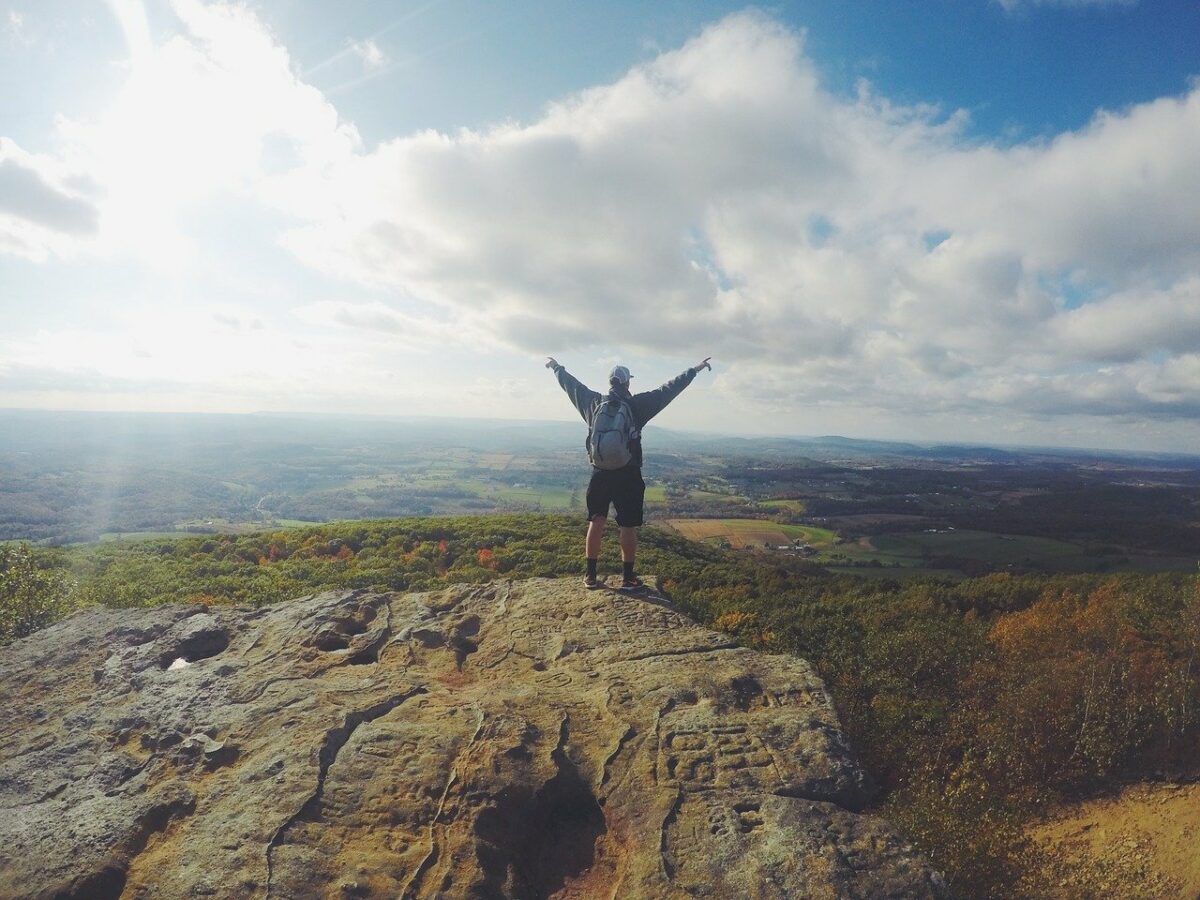mountain top experience person holding arms up in the air in victory