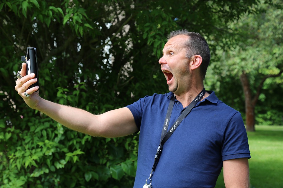 Picture of man looking at his phone from a distance with a very surprised, wide open mouth