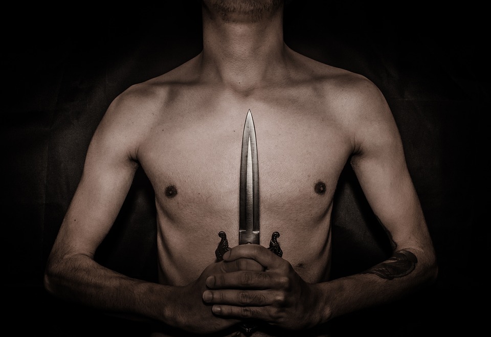 bare chested man holding a dagger in front of him