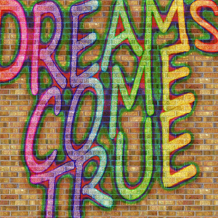 Graffiti like letters on a brick wall background that say: "DREAMS COME TRUE"