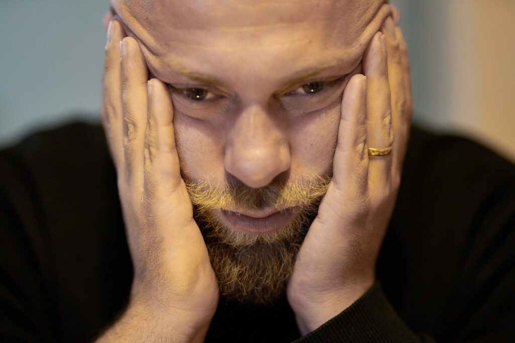 man with his hands holding his face with expression of apparent desperation