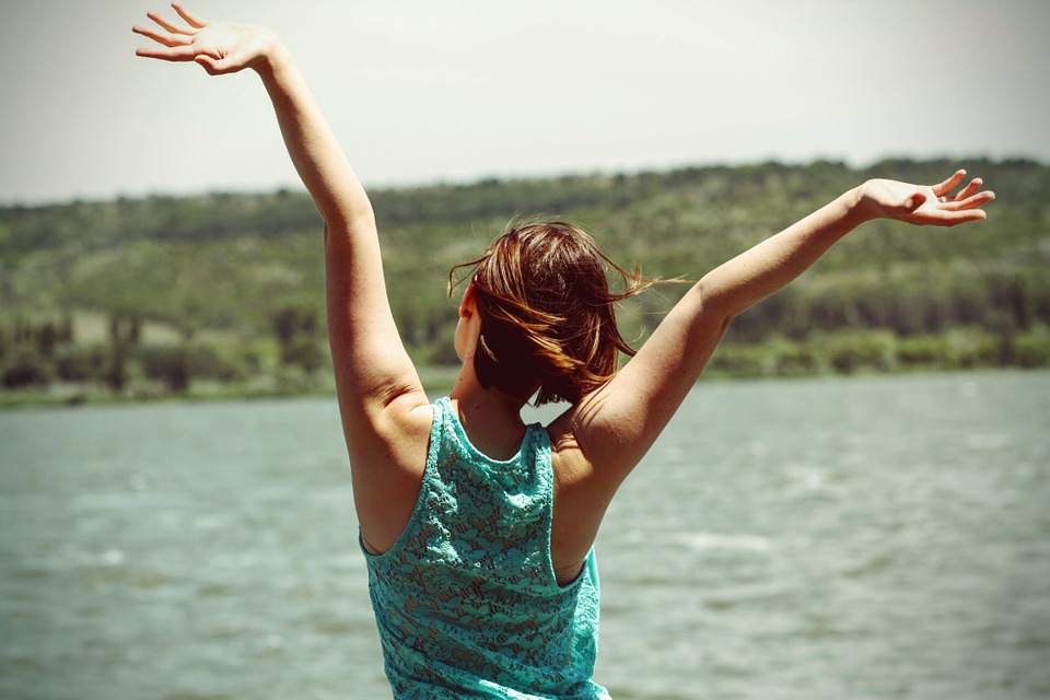 girl looking over the water with her arms up in the air as if in joy for knowing her purpose