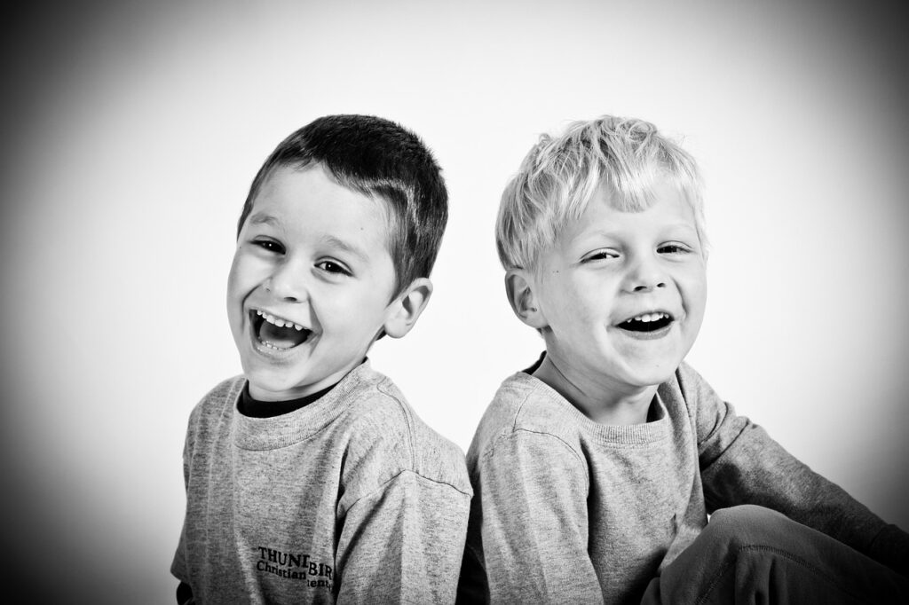 Two young boys sitting together with big smiles laughing and being merry