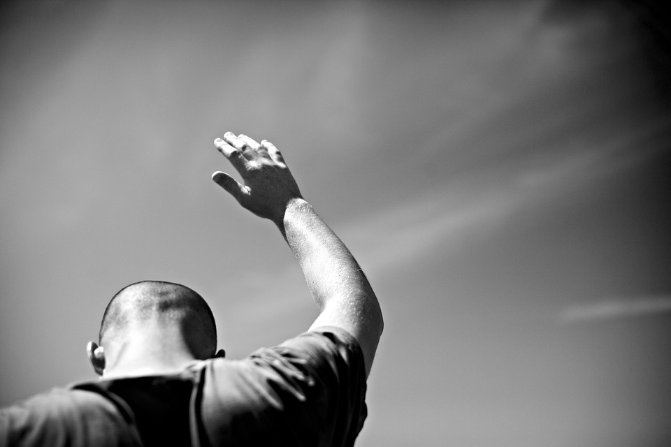 man facing away from camera with right arm extended up in offering with sun rays beaming off of him
