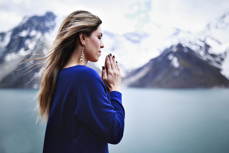 woman praying with mountains blurred out in the background