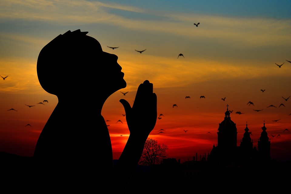 praying while looking up with sunset in the background