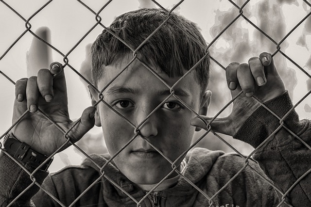 black and white picture of poor looking boy behind fence