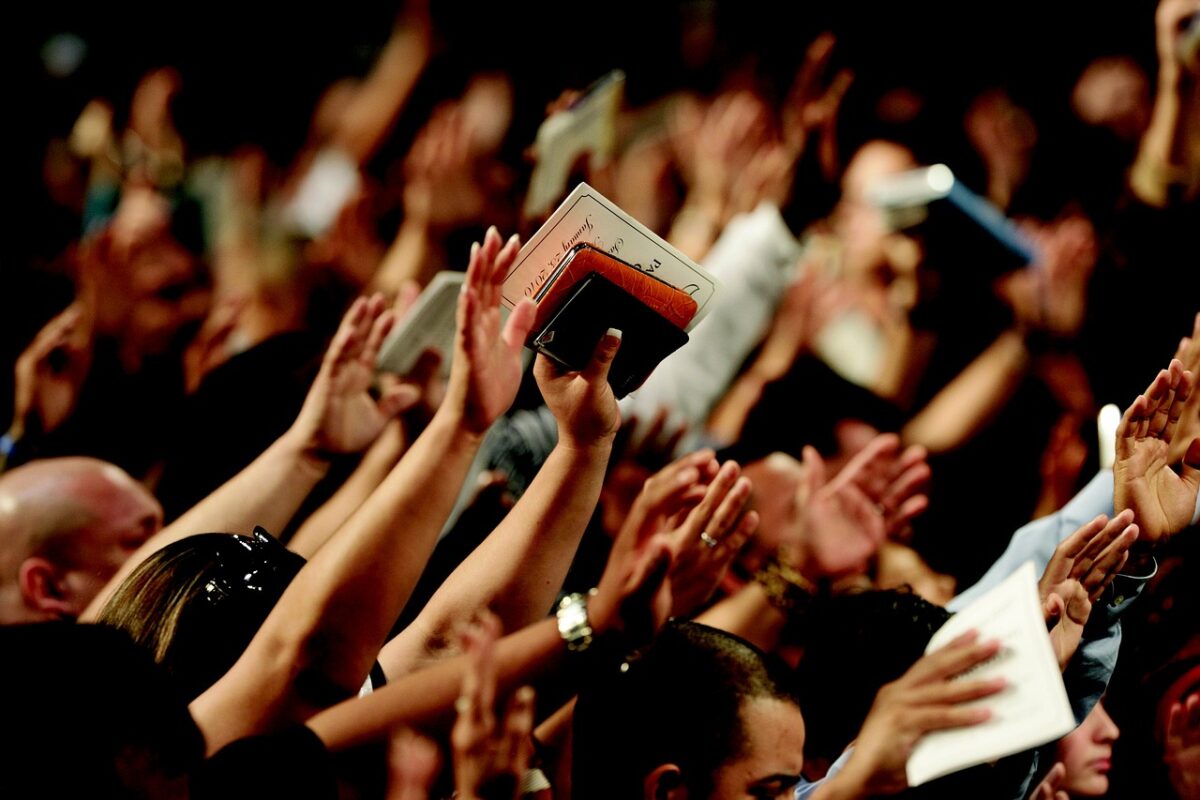 crowd worshipping with arms in the air, holding Bibles