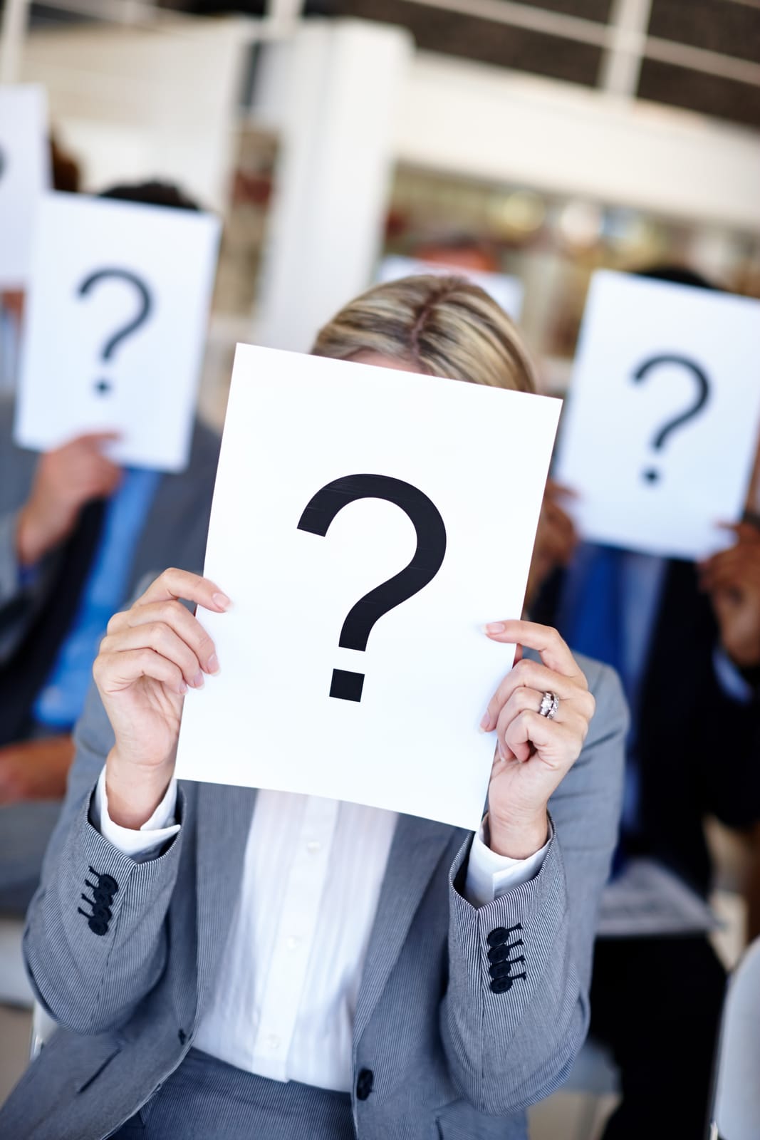 a person in a group of people holding up question marks on paper in front of their faces
