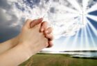 praying hands with sunbeams around cross in the background